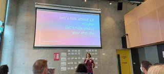 Fiona MacNeill is shown presenting to a large room, with the slide title projected above reading, Let’s talk about LX maybe, Let’s talk about you and me
